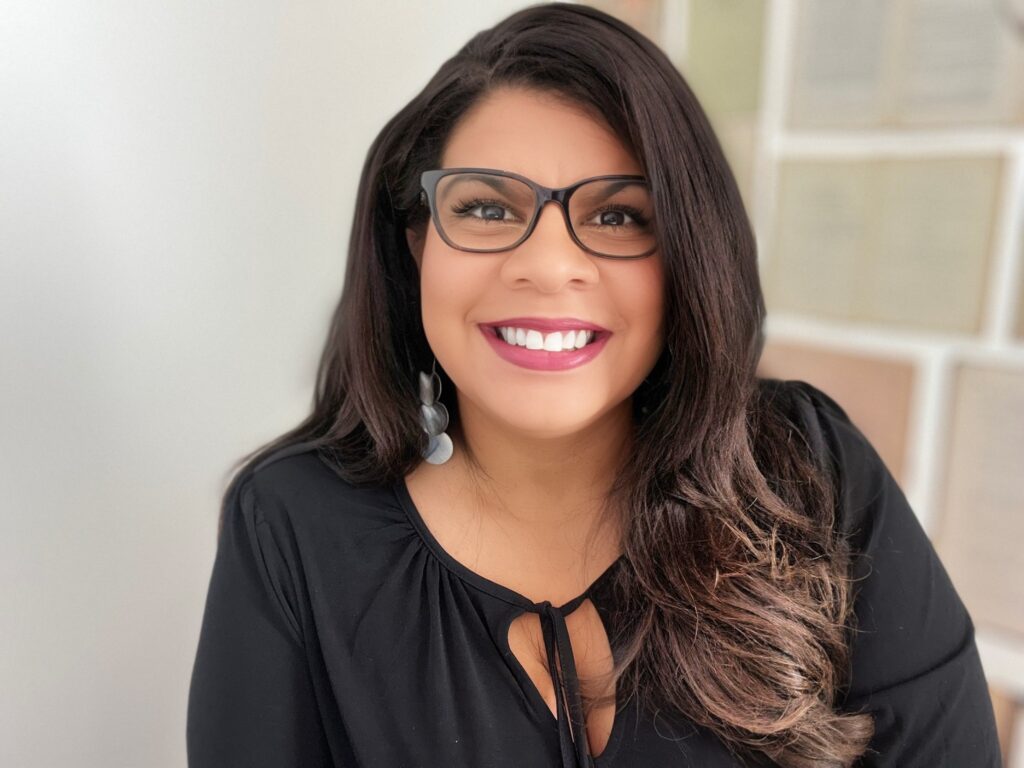 Alicia Lyttle smiling in a professional setting, framed by certificates and documents, representing leadership in AI consulting for businesses.